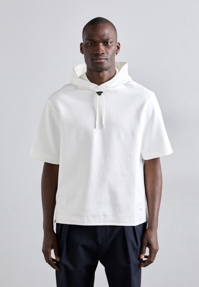 White short-sleeve hoodie with a drawstring at the neck, made from soft fabric. Features a rounded hem and subtle logo accent at the side.