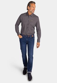 Overhemd met een donker patroon, gecombineerd met blauwe spijkerbroeken. De outfit wordt compleet gemaakt met donkere sneakers en een bruine riem.