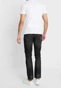 Sorte denim jeans med lige ben, baglommer og kontraststing, parret med en simpel hvid t-shirt og hvide sneakers.