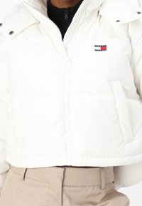 Vit puffjacka med kort design, dragkedja framtill och sidofickor. Inkluderar en logotyp-patch på vänstra bröstområdet.