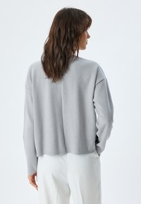 Felpa grigia corta con finitura testurizzata, spalle cadute e una cucitura sottile lungo la schiena, abbinata a pantaloni bianchi.