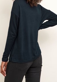 Haut à manches longues bleu marine avec une coupe décontractée, fentes latérales et texture douce, associé à un jean noir ajusté.