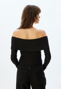Schwarzes, schulterfreies, geripptes Langarmoberteil mit schichtweise Design und figurbetonter Silhouette. Kombiniert mit hochtaillierten schwarzen Hosen.