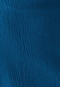 Tissu texturé d'une couleur turquoise vive, présentant un motif ondulé avec un léger éclat. Le matériau semble lisse et flexible.