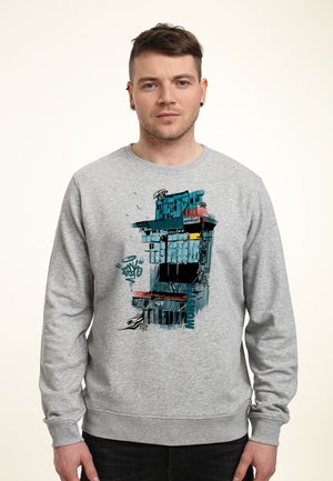Szara bluza z nadrukiem graficznym przedstawiającym budynek z niebieskimi i pomarańczowymi akcentami. Miękki materiał, ściągacze na rękawach i okrągły dekolt.