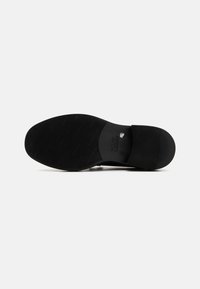 La suola nera delle scarpe presenta una superficie di gomma testurizzata con scanalature orizzontali e un tallone liscio. La stampa sulla soletta indica informazioni sul marchio.