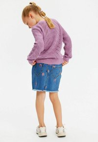 Lila stickad tröja med ett texturerat mönster, parat med en blå denimkjol med regnbågsbroderi och fransad nederkant.