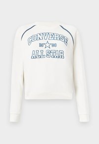 Sweat-shirt à col rond couleur blanc cassé avec un graphisme bleu « CONVERSE ALL STAR 1908 ». Présente des manches raglan et des poignets côtelés, avec une texture de tissu lisse.