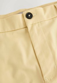 Ceinture de pantalon beige avec un bouton noir attaché à travers une boutonnière cousue sur un tissu lisse.