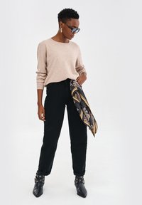 Jasno beżowy sweter, czarne spodnie z wysokim stanem, czarne botki za kostkę z dodatkowymi elementami, oraz czarny szalik z misternym wzorem w złocie i szarości.