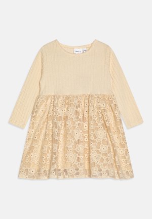 Langærmet kjole til småbørn i cremefarve med tekstureret strikket top og blomsterblonde nederdelsoverdel, der har rund halsudskæring og indsamlet talje.
