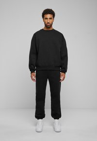Felpa nera e pantaloni abbinati in tessuto morbido. Collo a giro, vestibilità comoda, polsini a costine e pantaloni lunghi fino alle caviglie. Sneakers bianche.