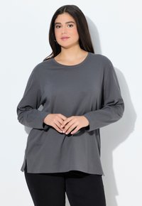 Grijze lange mouw shirt, ronde halslijn, zachte stof, zijsplitten aan de zoom, gecombineerd met zwarte broeken. Eenvoudig ontwerp, geen zichtbare patronen of hardware.