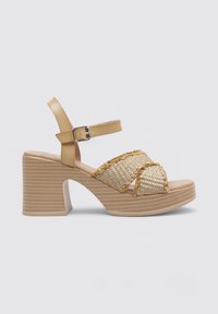 Beige block-heeled sandal with tan leather straps, woven jute upper, and decorative fringed detailing. Textured platform sole.