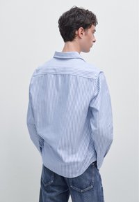 Camicia a righe in cotone azzurro chiaro e bianco, con colletto a punta e maniche lunghe, dal taglio morbido e orlo curvo sul retro.