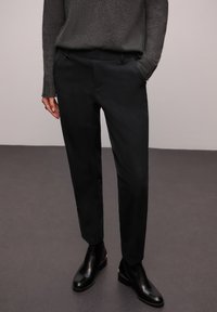 Czarne spodnie o dopasowanym kroju z gładką fakturą materiału, wyposażone w boczne kieszenie i gładki przód. Noszone z czarnymi botkami do kostki.