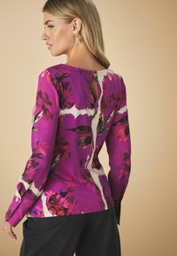 Pitkähiha blouse kirkkaan violetissa värissä, jossa on kukkakuosi ja selässä avainreikäyksityiskohta. Valmistettu sileästä kankaasta, jossa on istuvat hihat ja muotoiltu leikkaus.