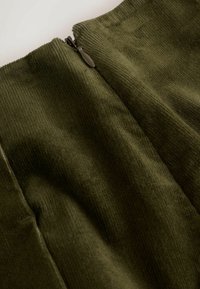 Olíva zöld kordbársony anyag függőleges bordákkal, oldalsó cipzárral. Puha tapintású és sima felületű, tiszta széllel.