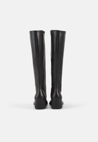 Juodos odos ilgi batai iki kelių su lygiu paviršiumi, vertikaliu siluetu, blokiniais kulnais ir užtrauktukais gale, užtikrinančiais lengvą avėjimą.