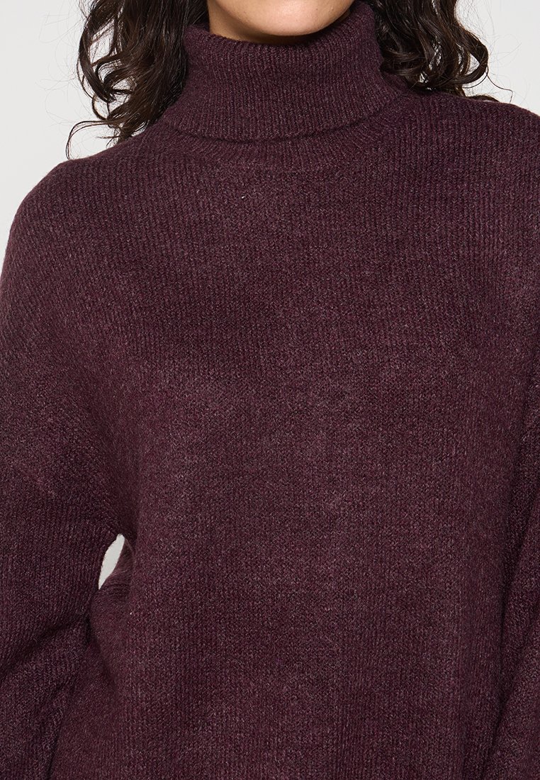 Pull à col roulé bordeaux en matière tricotée douce et texturée, avec un design ample et un col côtelé.