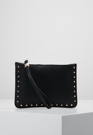 Schwarze strukturierte Wristlet-Clutch mit goldenen Nieten entlang der Kanten und einem schmalen Riemen in der Nähe des Reißverschlusses, auf einem weißen Podest präsentiert.