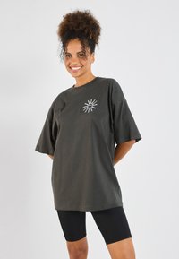 Dark green oversized t-shirt made of cotton with short sleeves, featuring a white sun graphic on the chest and paired with black leggings.