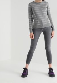 Grau gestreifter Pullover mit Rundhalsausschnitt, kombiniert mit schlanken grauen Jeans und schwarz- lila Sneakers mit einer strukturierten Sohle.