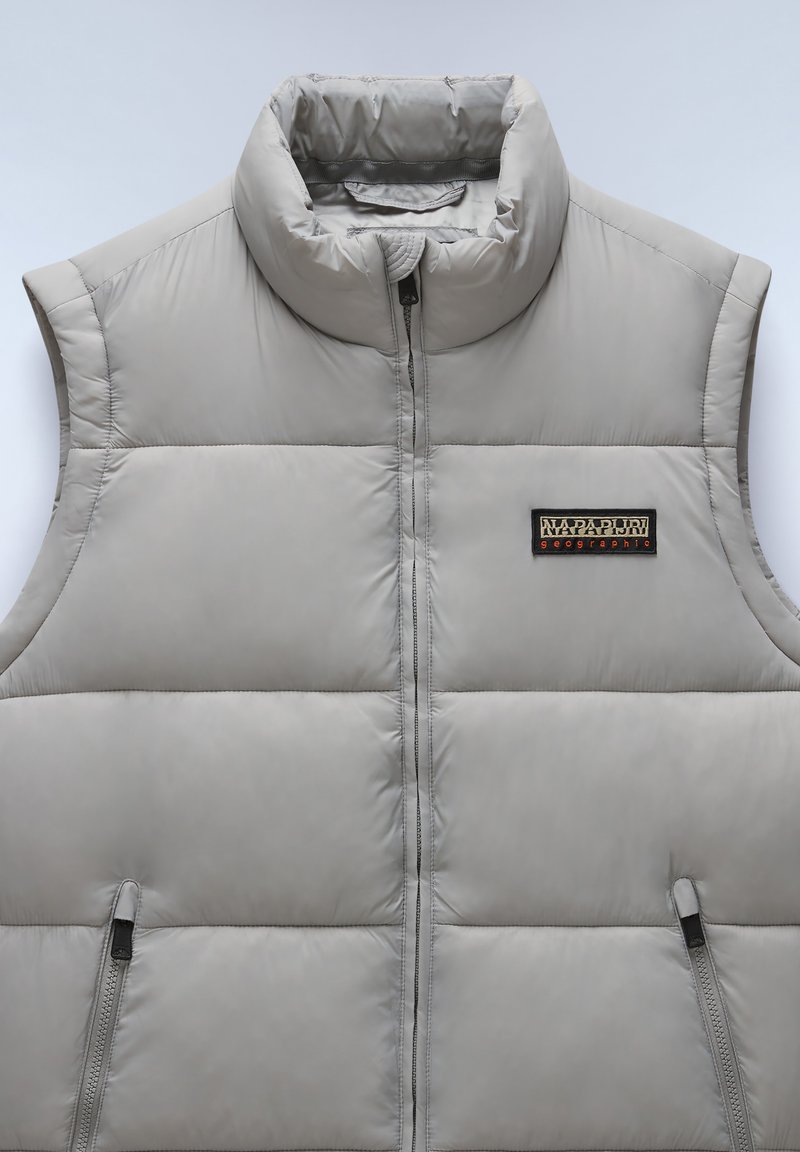 Ljusgrå ärmlös puffer-väst med hög krage, vertikal quiltning och en zippered ficka, med en märkespatch på vänster sida.