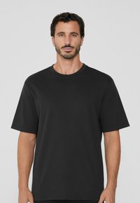 T-shirt noir à manches courtes en coton doux. Il présente un col rond classique, une coupe décontractée et une texture légère.