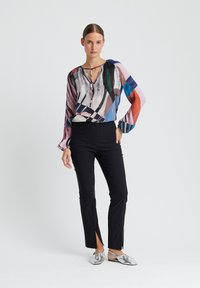 Blouse à motifs multicolores avec des manches longues, décolleté en V profond et cordon de serrage. Associée à un pantalon noir ajusté avec des fentes latérales et des chaussures argentées.