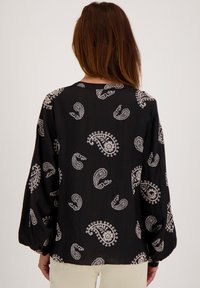 Zwarte blouse met wit paisleypatroon, lange ballonmouwen en een losse pasvorm. Gestructureerde stof met een subtiele glans en afgeronde zoom.