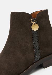 Stivale alla caviglia in suede marrone con un dettaglio intrecciato nero sul lato e un'etichetta dorata con incisione "See By Chloé".
