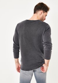 Dunkelgraues Langarmshirt mit runder Ausschnitt und strukturiertem Stoff. Das Shirt hat einen lässigen Schnitt und verfügt über umgeschlagene Ärmel.