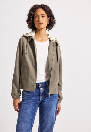 Licht olijfgroene zip-up jas met een crèmekleurige capuchon, elastische manchetten en zijzakken. Gekocht over een wit shirt en een blauwe spijkerbroek.