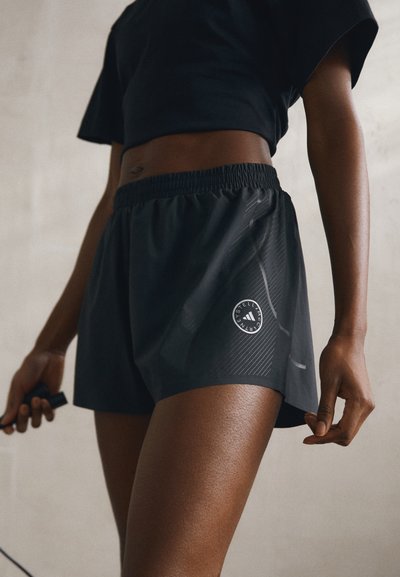 Pantaloni sportivi neri con cintura elastica, dotati di un logo e strisce diagonali. Il materiale sembra leggero con una texture liscia.