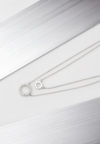 Collana in argento a due strati, uno con un ciondolo circolare tempestato di piccole pietre trasparenti e l'altro con un accento circolare semplice.