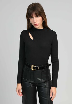 Haut noir à manches longues avec une découpe unique sur l'épaule, assorti à un pantalon en cuir noir taille haute et une boucle de ceinture dorée.