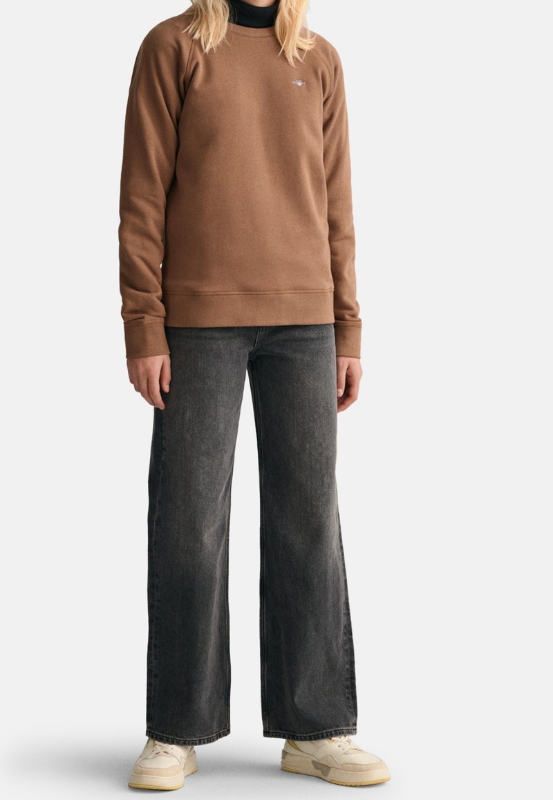 Brązowy polarowy sweter z okrągłym dekoltem, ściągaczami przy mankietach i u dołu. Połączony z szerokimi szarymi dżinsami i jasnymi trampkami.