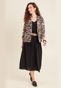 Multicolored bloemenpatroon blazer over een zwarte jurk, cinched met een beige riem, aangevuld met zwarte loafers en ronde oorbellen.