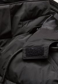 Black fabric with a subtle grid pattern, featuring a velcro patch and a drawstring element, showcasing a smooth, textured finish.