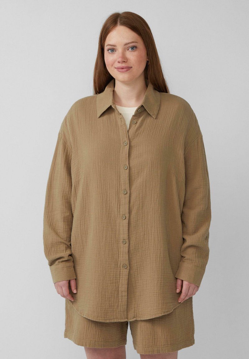 Lichtbruine button-up shirt van een textuur katoen stof, met een kraag, lange mouwen en een gebogen zoom. Korte bijpassende broeken zijn zichtbaar.