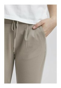 Beige joggebukser med en myk tekstur, elastisk snor i livet og sidelommer, kombinert med en hvit, litt cropped topp.