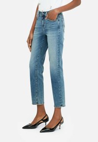 Hele helesinise denim püksid kitsas sirge lõikega, viie taskuga ja peene pleekimisega, koos mustade teravatipuliste kontsakingadega.