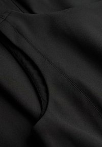 Zwarte stof close-up met een gladde textuur; bevat zichtbare stiksels en een gebogen opening, wat aangeeft dat het een zak of decoratief detail is.