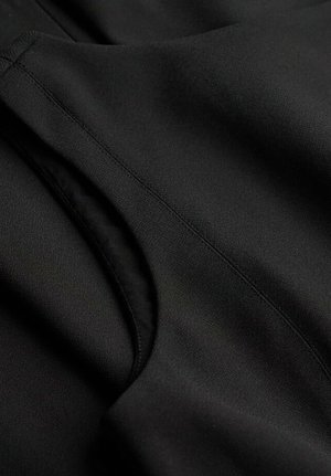 Primer plano de una tela negra con una textura suave; presenta costuras visibles y una entrada curva, indicando un bolsillo o un detalle decorativo.