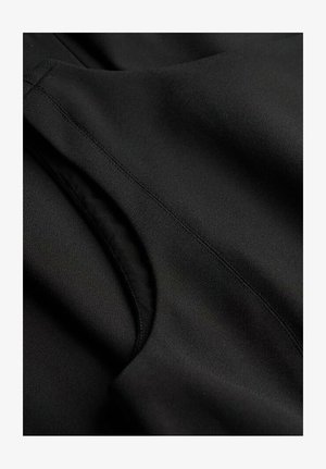 Zwarte stof close-up met een gladde textuur; bevat zichtbare stiksels en een gebogen opening, wat aangeeft dat het een zak of decoratief detail is.