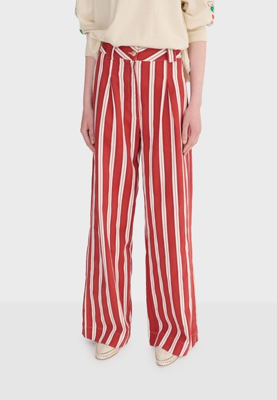 Pantalon large à rayures verticales rouges et blanches porté avec un haut beige et des chaussures pointues crème sur un fond clair.