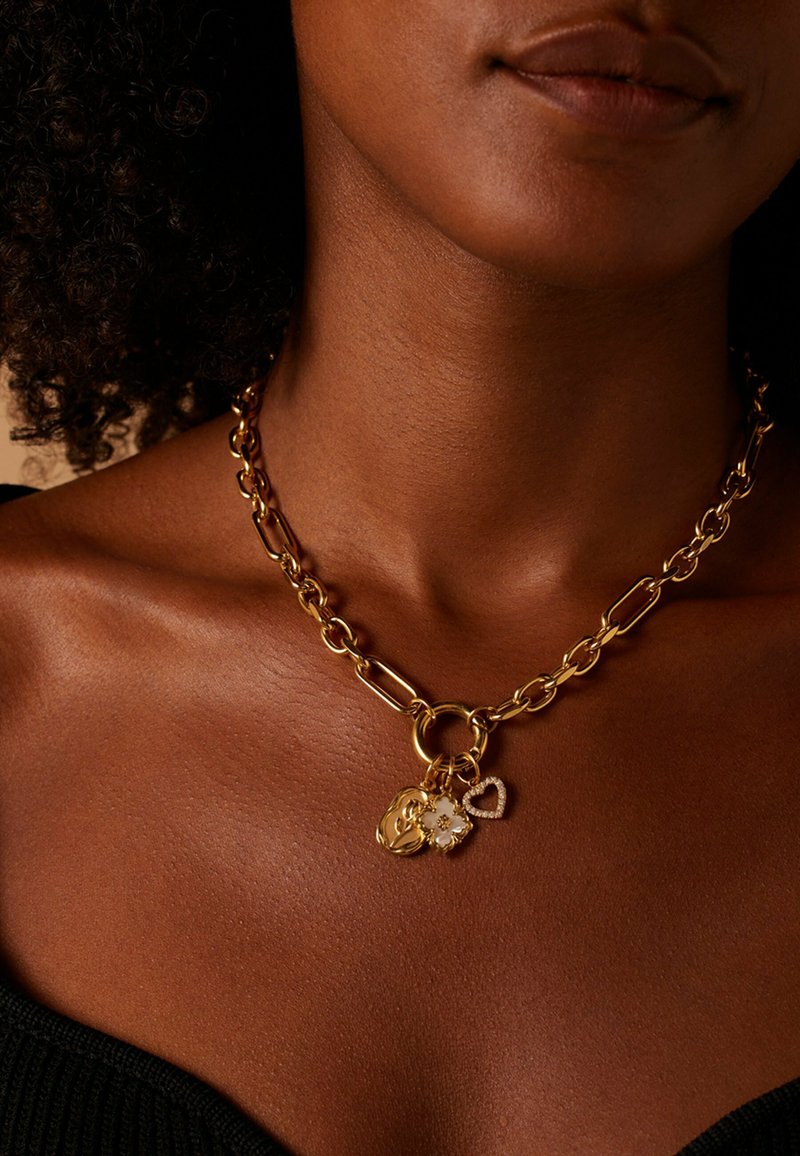 Gouden ketting met grote schakels, een ronde sluiting en drie bedels: een bloemblaadje, een hart en een gestructureerde hanger.