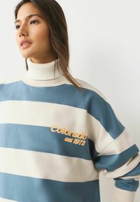 Color-blocked sweatshirt with horizontal blue and cream stripes. Features a high ribbed neckline and embroidered "Colorado est 1972" detail.