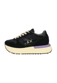 Baskets noires avec un mélange de matériaux texturés, lacets crème, accents violets sur la semelle et un détail de talon noir brillant.